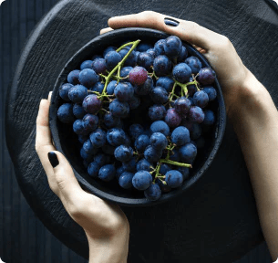 Black Grapes in black bowl being held by woman 